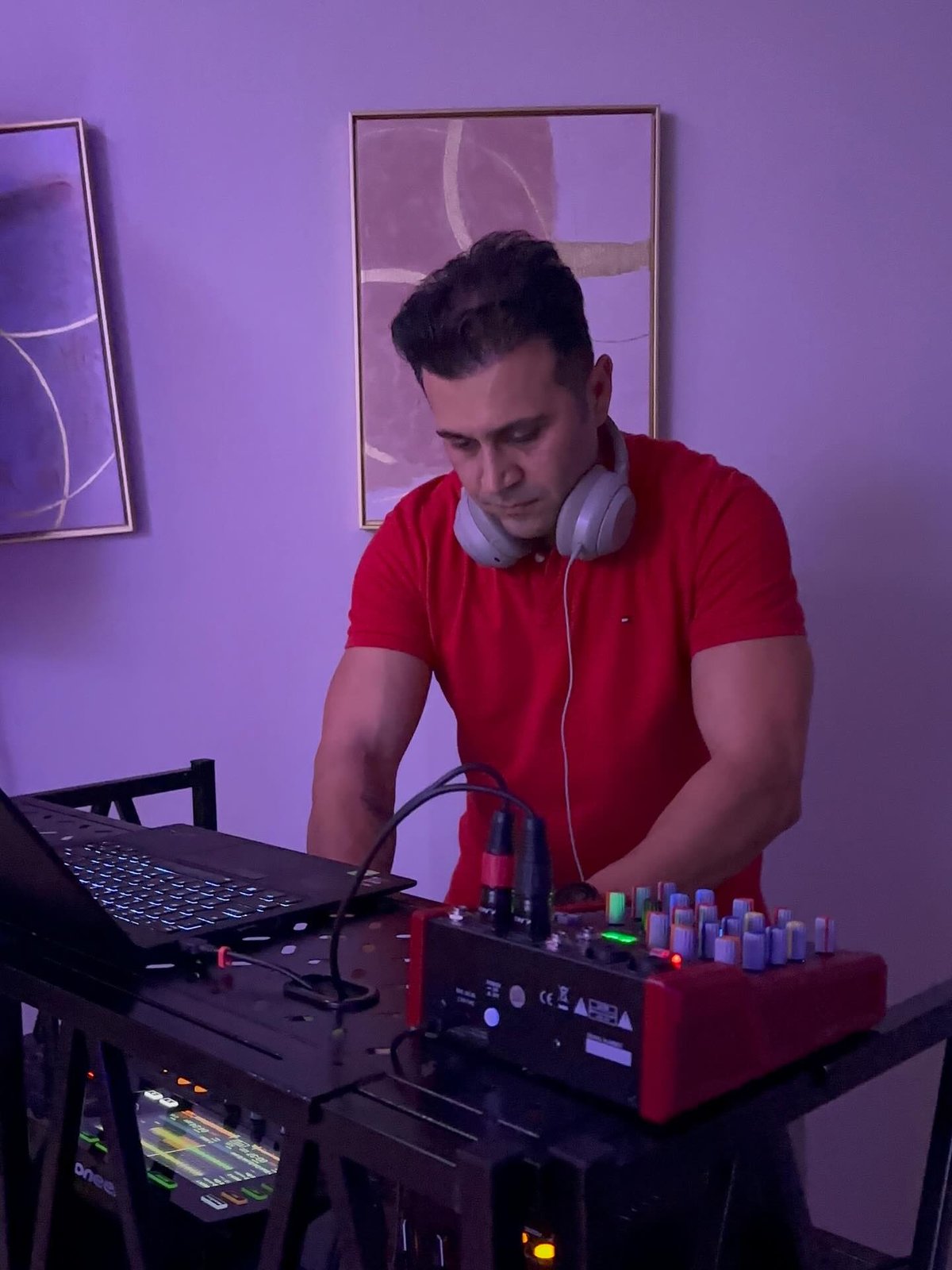 DJ Alphire behind the decks with headphones under purple event lighting.