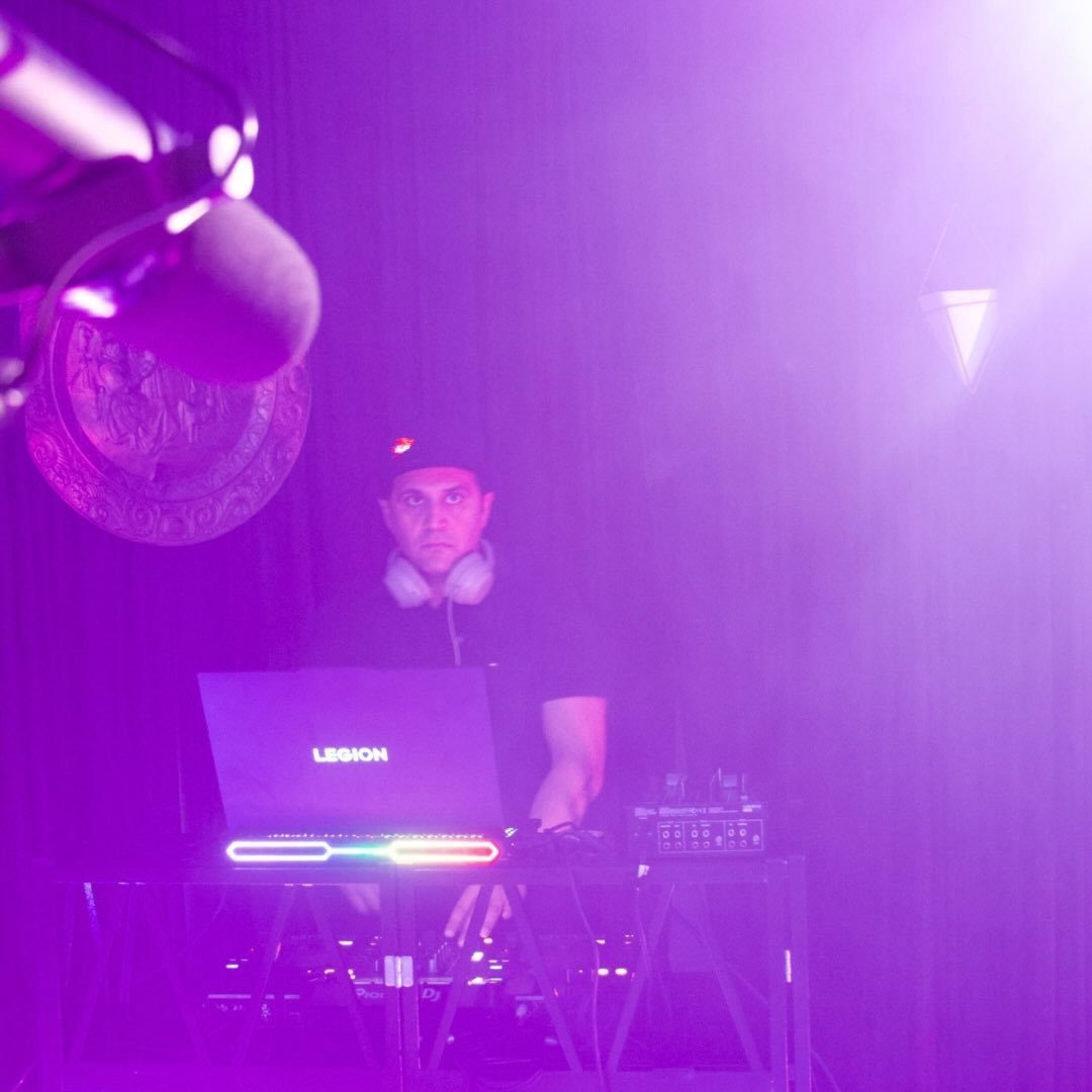 DJ Alphire performing under purple lights with his laptop and mixer