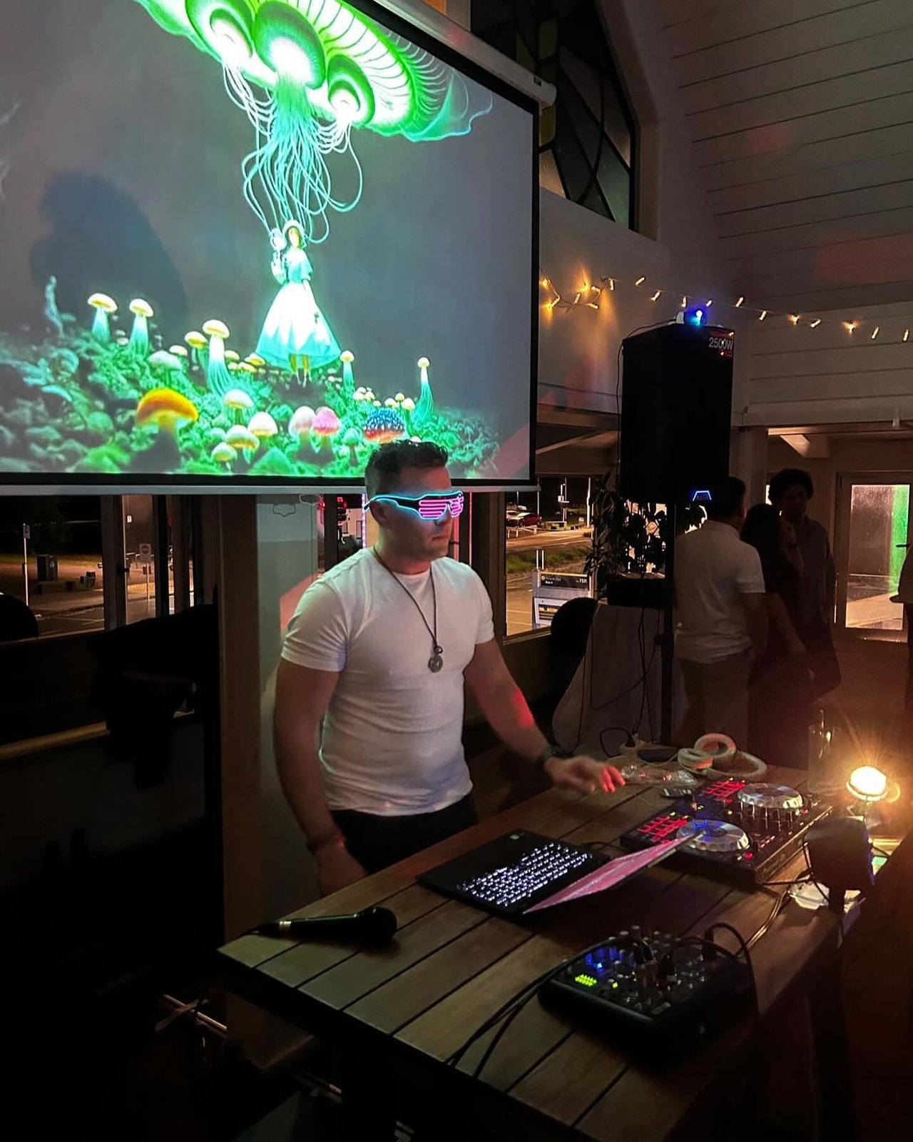 DJ Alphire performing with LED glasses and colorful projected visuals at a live event.